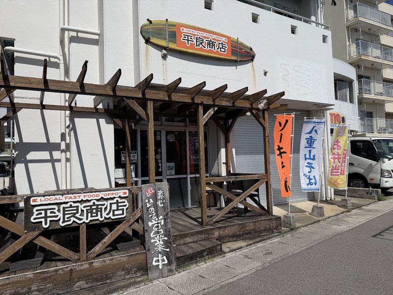 通りから見た平良商店。木のテラスとのぼり、サーフボード形の看板