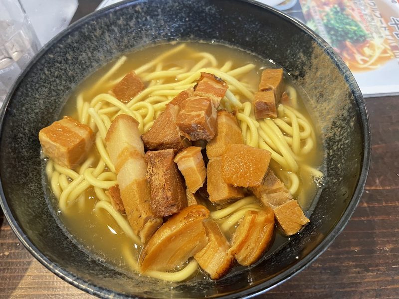 黒い器の黄色い麺に、角切りの豚肉をのせたそば