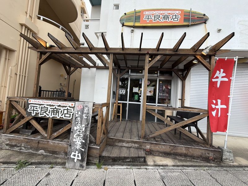 サーフボード形の「平良商店」の看板と木のテラスがある平良商店の店先