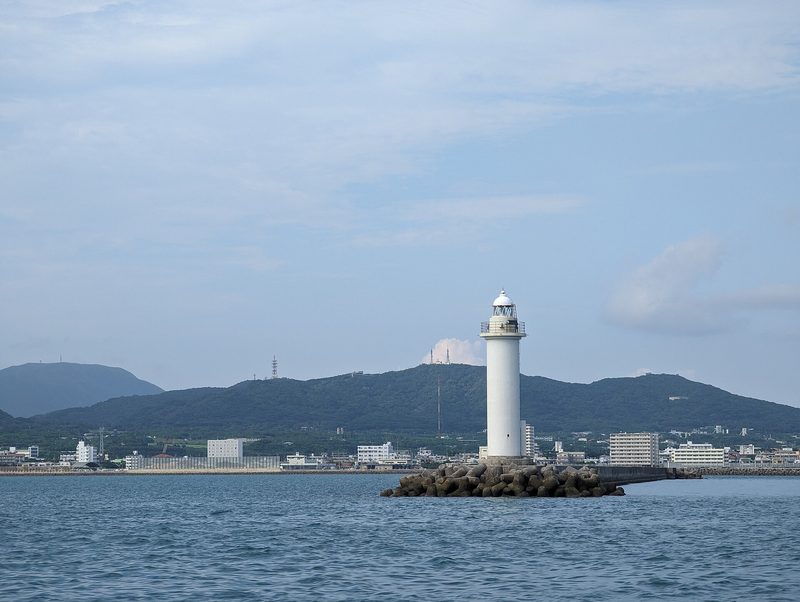 石垣港の入口に立つ白い灯台と、その奥の緑の山並み